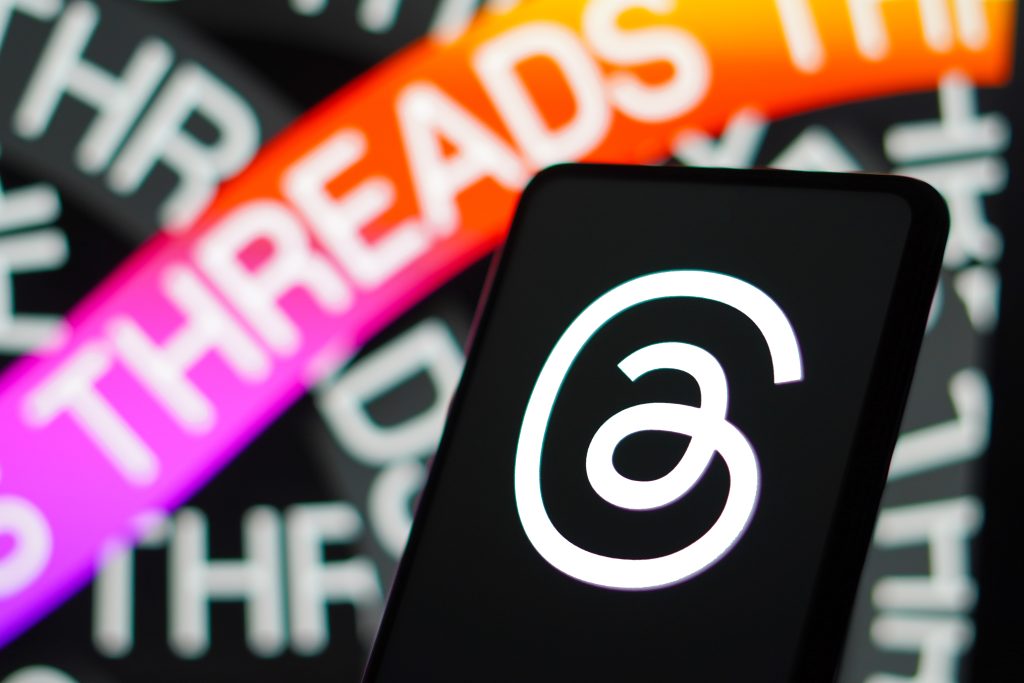 Phone with threads logo on it with threads text repeated in background